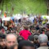 Multitud de personas en el mercado de El Rastro en la calle Embajadores de Madrid. A los lados, los puestos con mercancías del mercado, al fondo los árboles de la calle, y en primer plano un niño a hombros de espaldas.