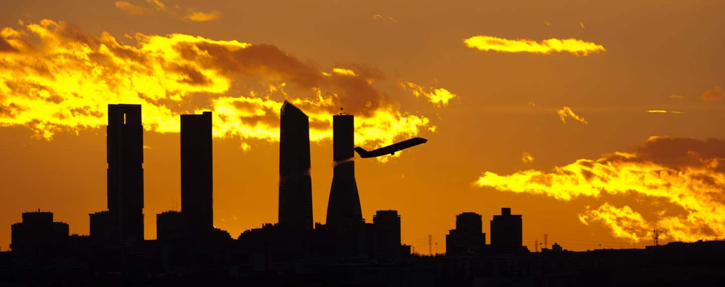 A plane departs from Adolfo Suárez Madrid-Barajas airport, the Cuatro Torres Business Area in the background (Madrid, Spain)