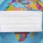 Salud global. Imagen de una mascarilla quirúrgica sujeta por dos manos y al fondo el globo terráqueo