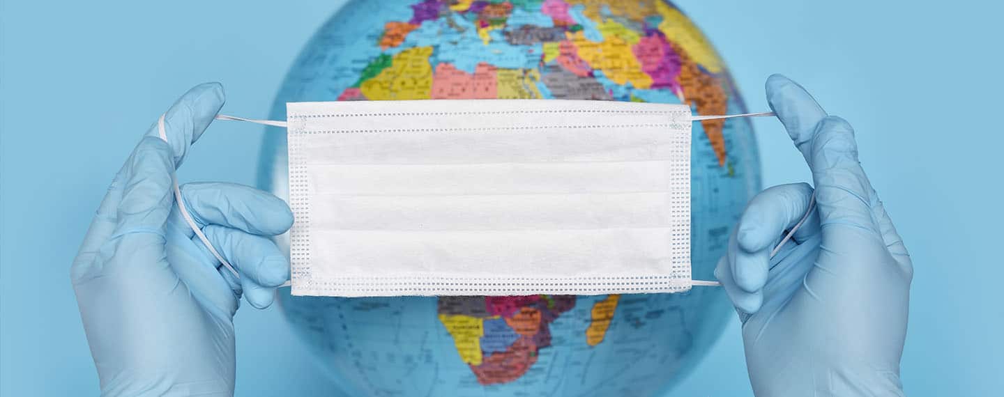 Salud global. Imagen de una mascarilla quirúrgica sujeta por dos manos y al fondo el globo terráqueo