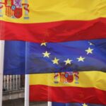 Imagen de las banderas de España y la Unión Europea con la sede del Ministerio de Asuntos Exteriores, de la Unión Europea y Cooperación al fondo