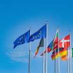 Dos banderas de la Unión Europea al centro acompañadas de banderas de países de Europa ondeando sobre un fondo azul
