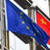 Mastiles con las banderas de la Unión Europea y China frente a un edificio con ventanales en Pekín.