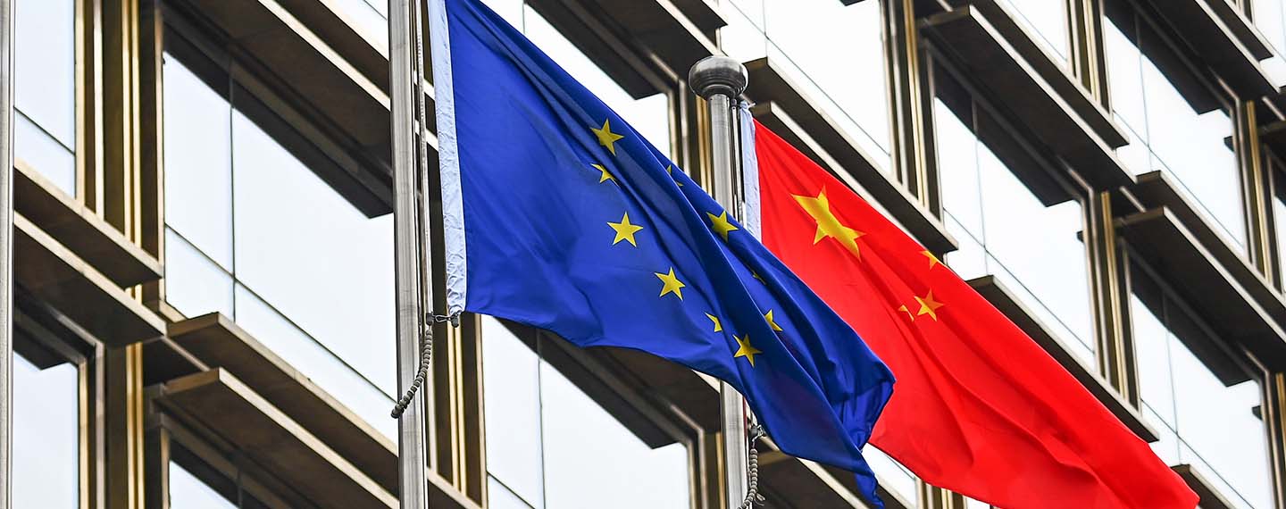 Mastiles con las banderas de la Unión Europea y China frente a un edificio con ventanales en Pekín.