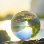 Cambio Climático. Bola de cristal sobre una roca oscura que refleja el paisaje de lago difuminado al fondo