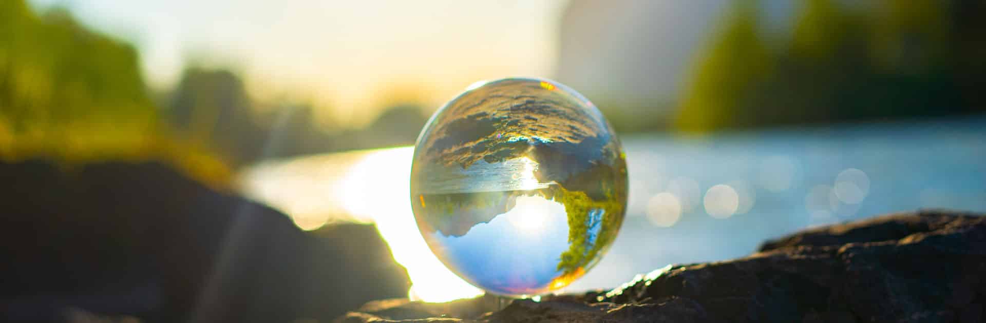 Cambio Climático. Bola de cristal sobre una roca oscura que refleja el paisaje de lago difuminado al fondo