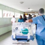 Personal de enfermería caminando por el pasillo de un hospital al lado de una incubadora con un bebé. Salud global