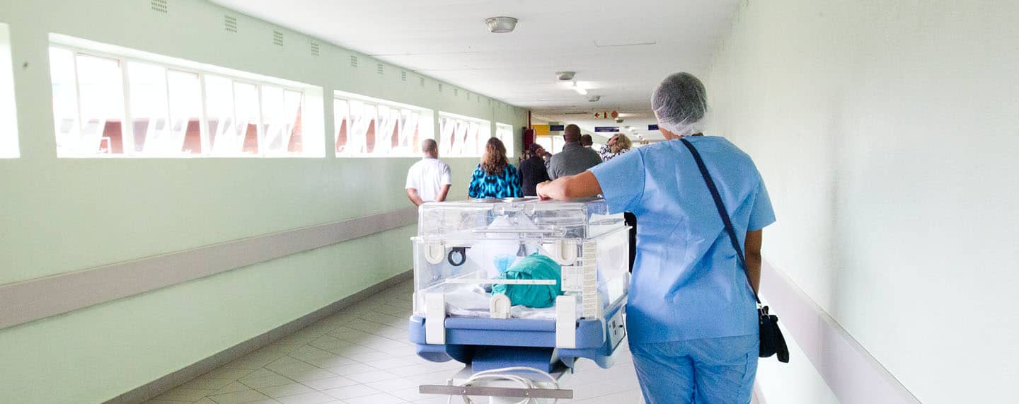 Personal de enfermería caminando por el pasillo de un hospital al lado de una incubadora con un bebé. Salud global