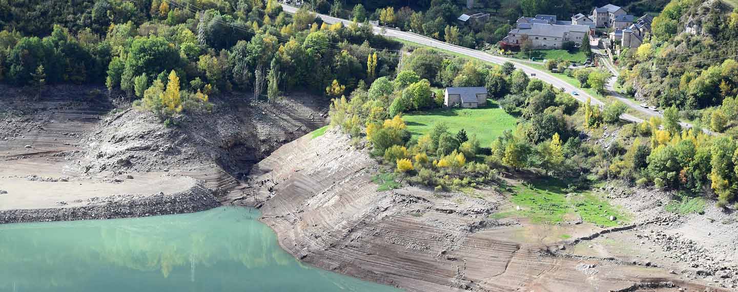 Imagen del embalse de Búbal ubicado en el Valle de Tena Huesca. En primer plano el agua del embalse en la ladera de la montaña, y al fondo una carretera comarcal con parte del núcleo urbano del pueblo de Búbal. Españoles ante el cambio climático