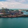 El enorme puerto logístico y comercial de Singapur, con un montón de grúas para mover contenedores, enormes barcos de carga en el fondo, centros comerciales y rascacielos en la isla de entretenimiento cercana. Economía mundial
