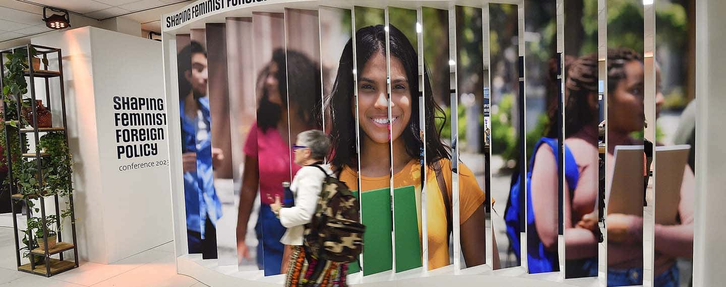 Una mujer de mediana edad con una mochila pasa frente a un panel de fotografías de la conferencia internacional sobre política exterior feminista Shaping Feminist Foreign Policy (SFFP), realizada en el Foro Mundial de La Haya en noviembre de 2023