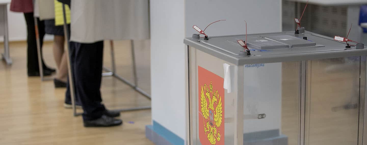 A la izquierda, personas de pies en las cabinas y a la derecha, unas urnas electorales con el escudo de la Federación Rusa en un colegio electoral durante las pasadas elecciones legislativas de 2021