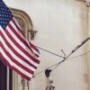 Banderas de Ucrania y Estados Unidos ondeando en un edificio. Fondo: Fachada de edificio con un balcón.