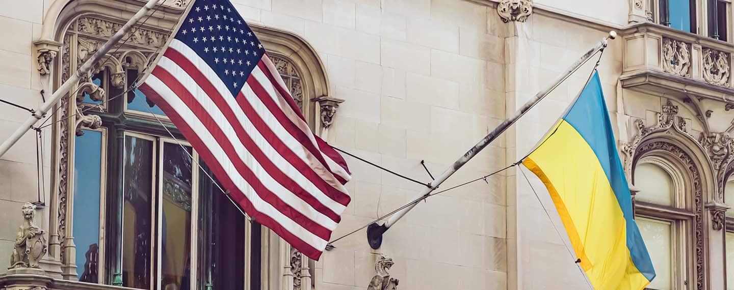 Banderas de Ucrania y Estados Unidos ondeando en un edificio. Fondo: Fachada de edificio con un balcón.