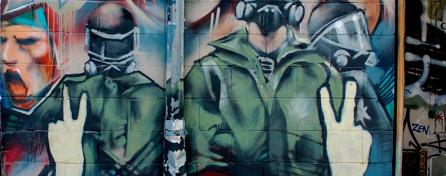 Graffiti detrás de Bloor West, cerca de la estación de metro Dundas West en Toronto (Canadá). El graffiti muestra en primer plan unas manos levantadas haciendo el símbolo de paz contra el fondo donde hay tres figuras enmascaradas que representan fuerzas militares y policiales y a la izquierda un rostro difuminado expresando un grito de ira