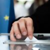 Person casting his vote in a ballot box. Background: Flag of the European Union.