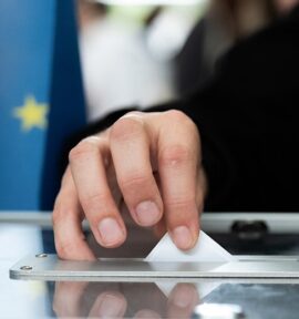 Person casting his vote in a ballot box. Background: Flag of the European Union.