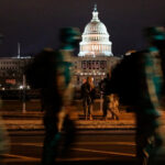 Imagen nocturna del Capitolio de Estados Unidos de noche. En primer plano, un grupo de soldados de la Guardia Nacional patrulla el perímetro. trump