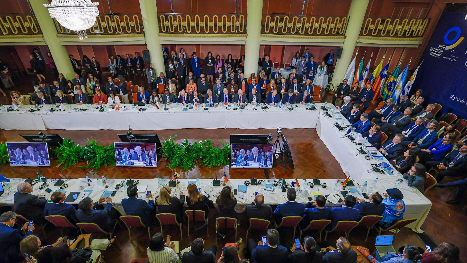 Detalle de la Cumbre de presidentes de los Estados Partes y Estados Asociados del Mercosur en Montevideo (Uruguay), donde los participantes están sentados alrededor de una gran mesa de conferencias en una sala formal, con las banderas de los países del Mercosur al fondo, el 6 de diciembre de 2024. UE-Mercosur