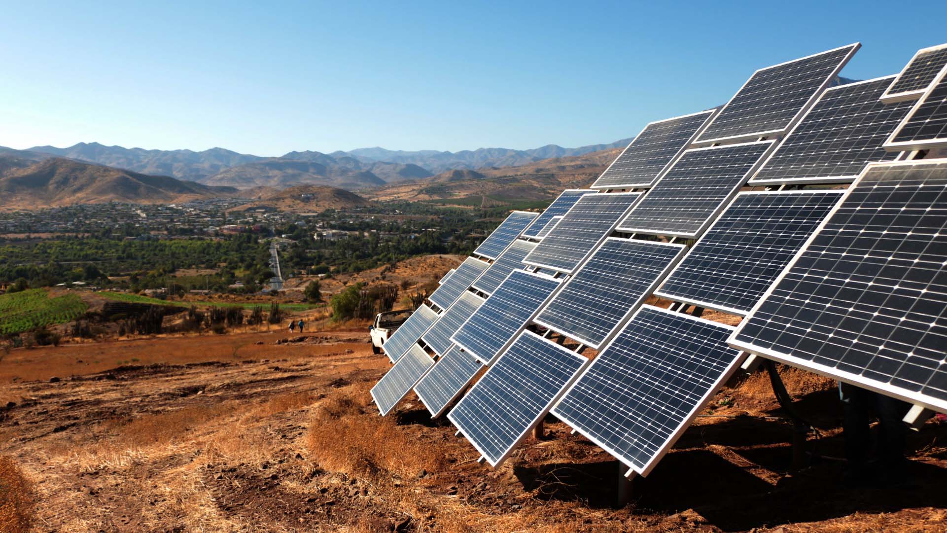 Filas de paneles solares instalados en una ladera cerca de Ovalle (Chile), en un paisaje rural con montañas al fondo y bajo el cielo azul despejado de Monte Patria. Transición energética