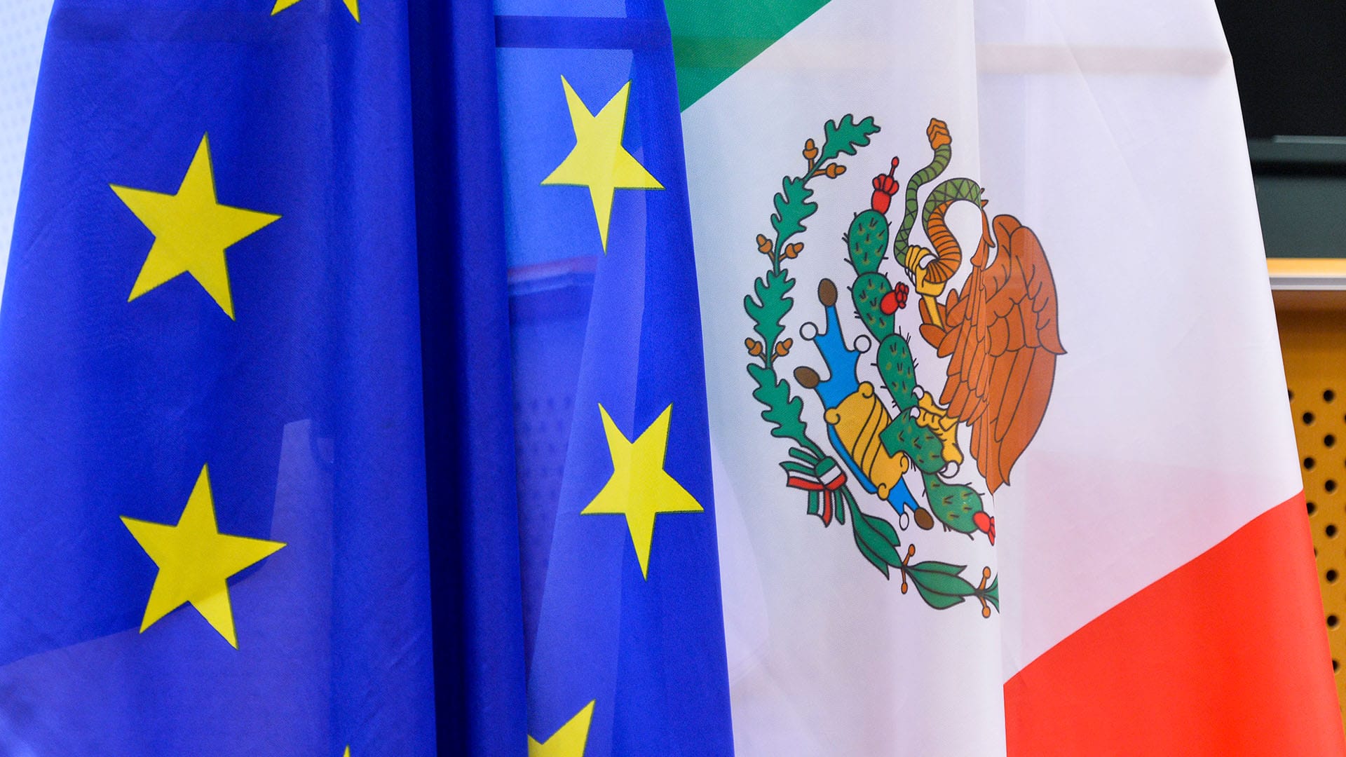 Banderas de la Unión Europea (azul con estrellas amarillas en círculo) y de México (tricolor con franjas verde, blanca y roja, con un escudo formado por un águila y una serpiente) en la XXV Reunión de la Comisión Parlamentaria Mixta México-Unión Europea de 2018. México