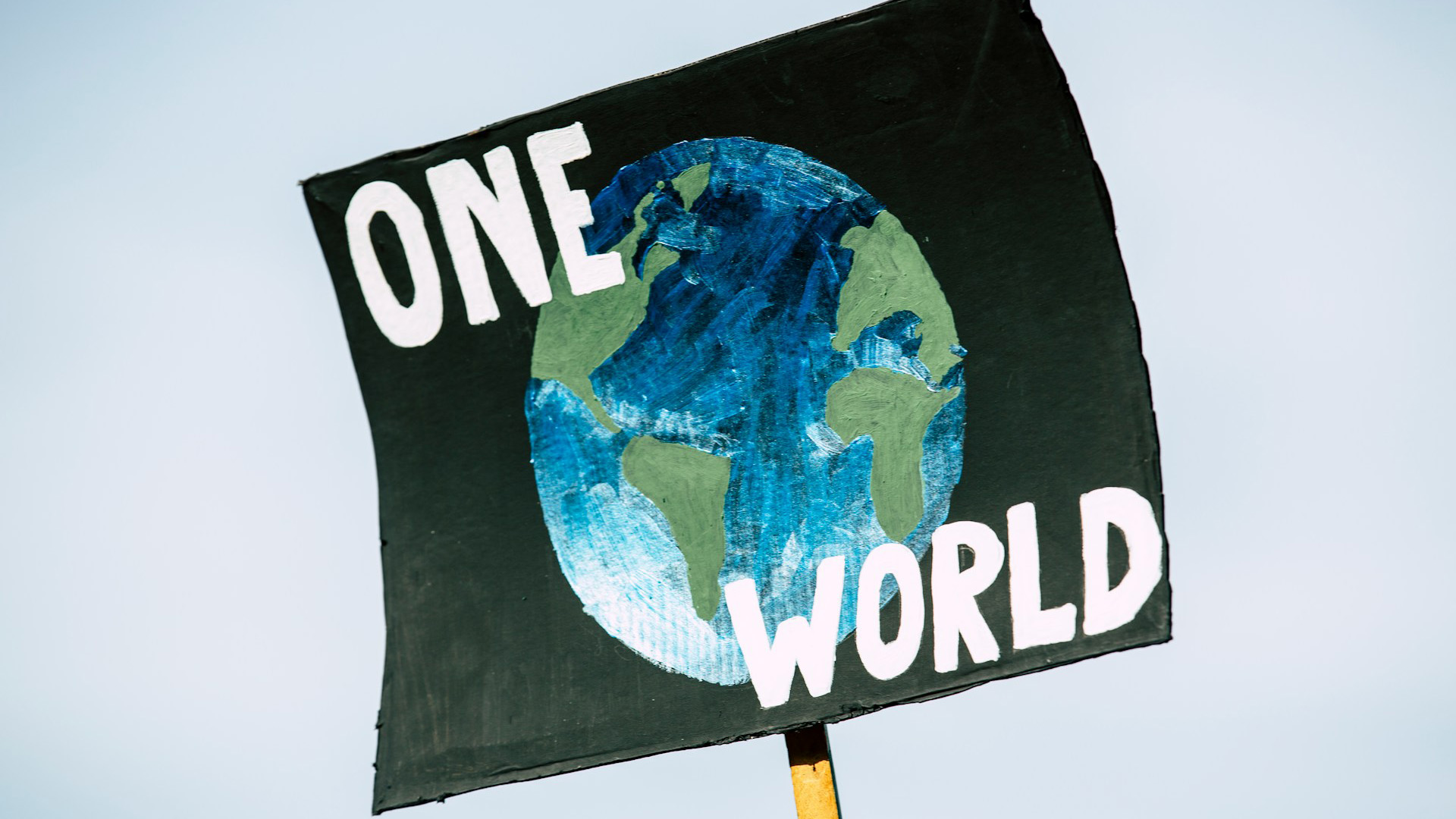 Hand-painted poster for the global climate change protest demonstration strike. On a black background, the representation of a globe in shades of green and blue with the words ‘One World’