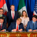 De izquierda a derecha, sentados y firmando el tratado de libre comercio entre EEUU, Canadá y México (USMCA) en la cumbre del G20 en Argentina en el año 2018: Enrique Peña Nieto, presidente de México, con un traje negro, camisa blanca y corbata a rayas rojas y azules; Donald Trump, presidente de EEUU, con un traje azul oscuro, camisa blanca y corbata roja; y Justin Trudeau, primer ministro de Canadá, con un traje, camisa y corbata en distintas tonalidades de azul. Al fondo, las banderas de Estados Unidos, Canadá y México, así como tres personas que acompañan la firma (dos hombres y una mujer de pie), con un fondo azul.