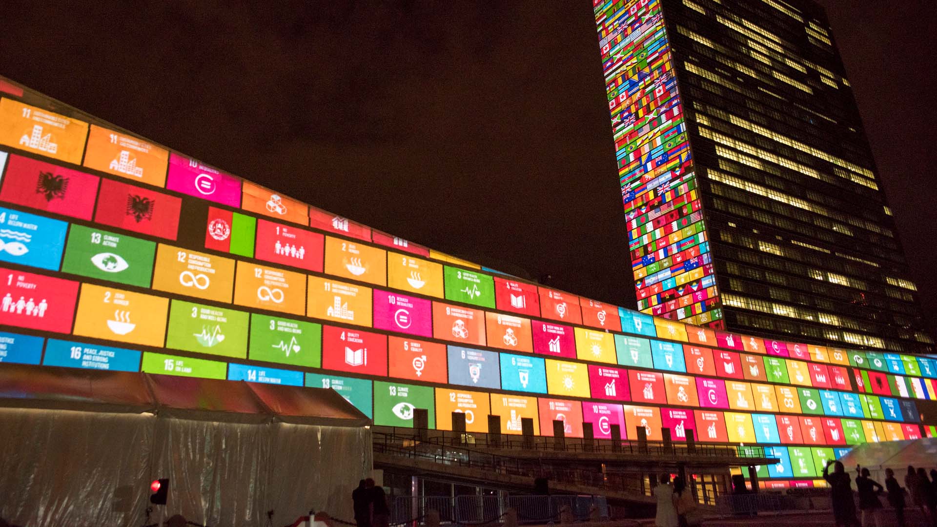 Nighttime projection on the United Nations Headquarters in New York City displaying the 17 colorful Sustainable Development Goals on the General Assembly building and a mosaic of world flags on the Secretariat tower, marking the UN’s 70th anniversary and promoting the 2030 Agenda for Sustainable Development. Private Capital Mobilisation