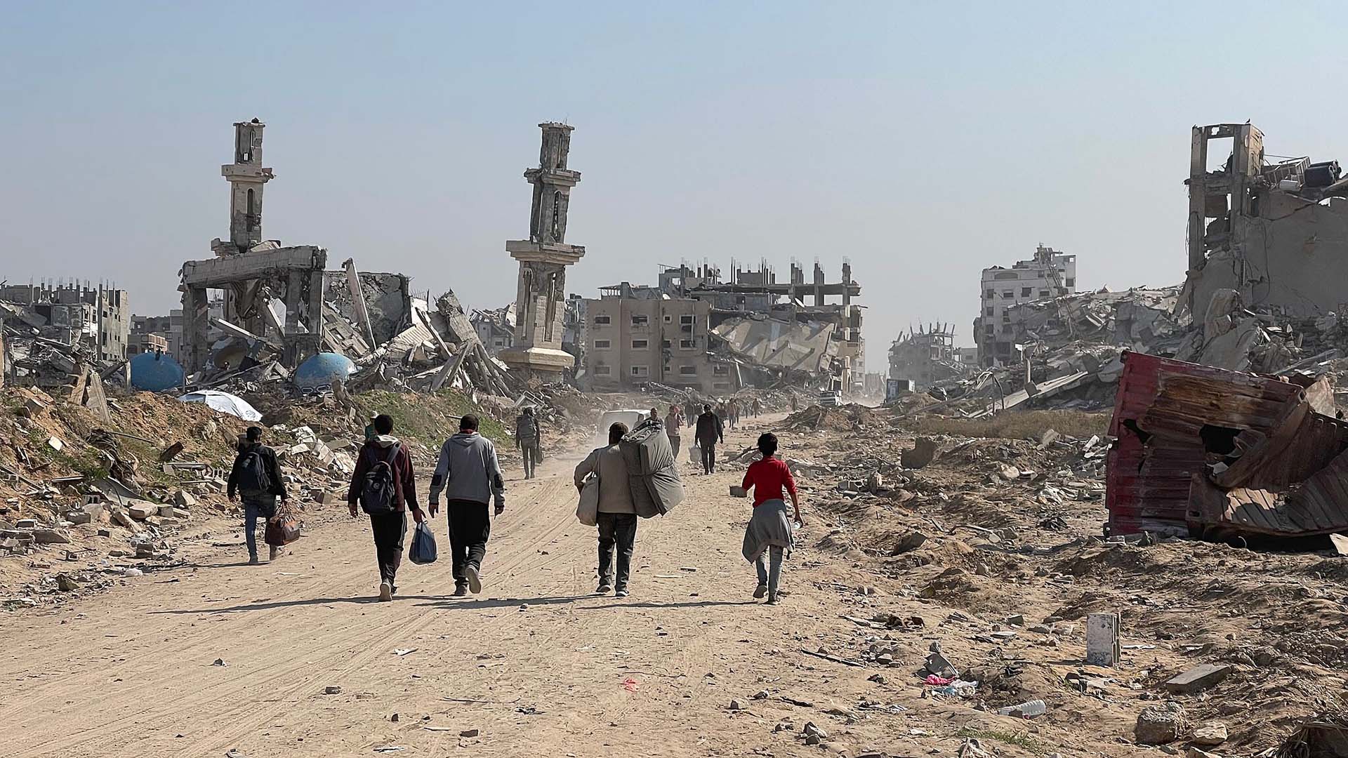 Grupo de personas caminando por una calle polvorienta entre escombros y edificios destruidos, en una zona de la Franja de Gaza gravemente afectada por el conflicto armado. Netanyahu