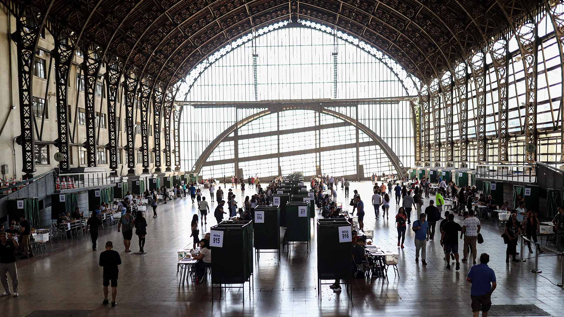 Chilean citizens vote during the second round of the 2024 regional elections in Santiago (Chile). The building is a metal-structured hall with a vaulted roof and large windows that allow plenty of natural light to enter. In the middle of the room, several voting booths are arranged in the centre of the hall. Latin America