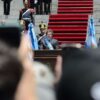 Javier Milei tras un podio mientras pronuncia su discurso frente al Congreso Nacional durante su investidura en 2023. Lleva la banda presidencial y la medalla, flanqueado por banderas argentinas y escoltado por miembros de la Guardia de Granaderos. A sus espaldas se extiende una alfombra roja sobre las escalinatas del Congreso, con numerosos asistentes y personal de seguridad alrededor.
