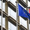 European Union and Chinese flags waving side by side in front of a modern glass building in Beijing. China