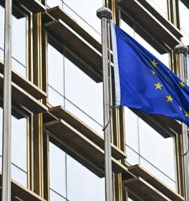 European Union and Chinese flags waving side by side in front of a modern glass building in Beijing. China