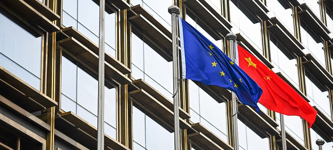 Banderas de la Unión Europea y de China ondeando lado a lado frente a un edificio moderno de cristal en Pekín. China