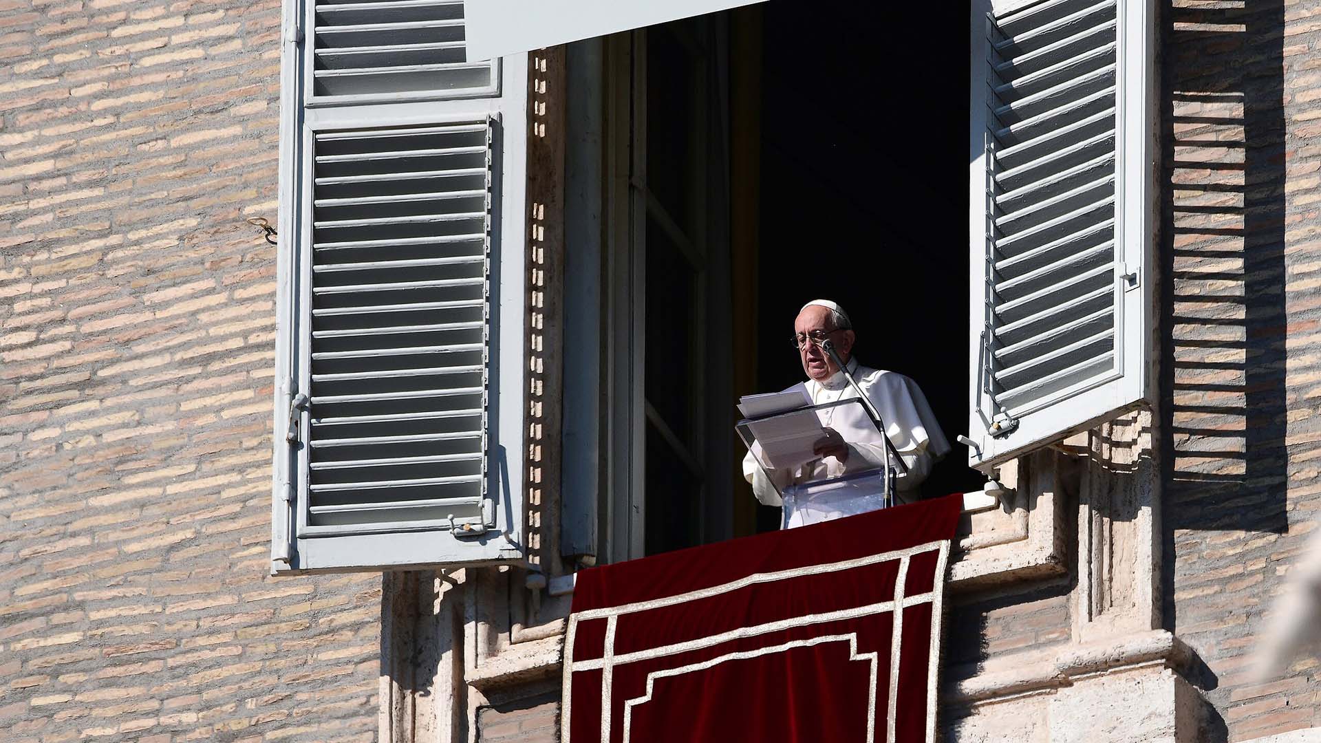 El Papa Francisco lee un discurso desde una ventana del Palacio Apostólico en el Vaticano durante el rezo del Ángelus, con una cortina roja decorativa colgando del alféizar. Vaticano