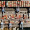 Vista aérea de un puerto marítimo industrial en Nápoles, con varias grúas de carga alineadas y contenedores de transporte multicolores organizados sobre el muelle y a bordo de un buque carguero atracado. UE