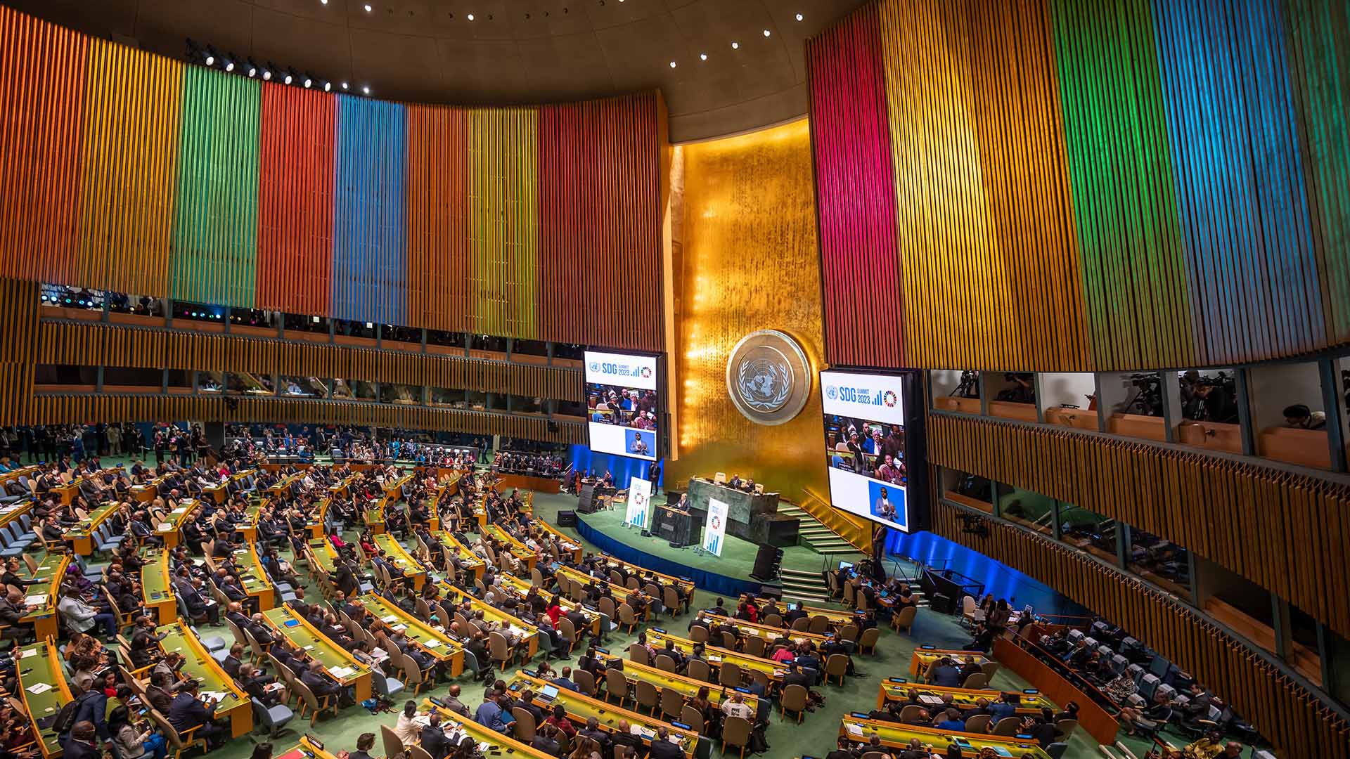 Vista panorámica del pleno de la Asamblea General de la ONU en Nueva York, con altos paneles verticales en colores brillantes que representan los Objetivos de Desarrollo Sostenible (ODS). António Guterres da un discurso durante la conferencia sobre los ODS, el 18 de septiembre de 2023. Foto: Michael Kappeler / picture Alliance / Getty Images
