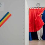 Una votante sale de una cabina de votación decorada con los colores rojo, amarillo y azul de la bandera de Rumanía durante la primera vuelta de las elecciones presidenciales de 2025. Rumanía