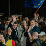 Presidential candidate Nicușor Dan greets his supporters after the first exit poll results during Romania’s presidential runoff election. A European Union flag and a Romanian flag can be seen among the crowd, while several people capture the moment on their mobile phones. Romania