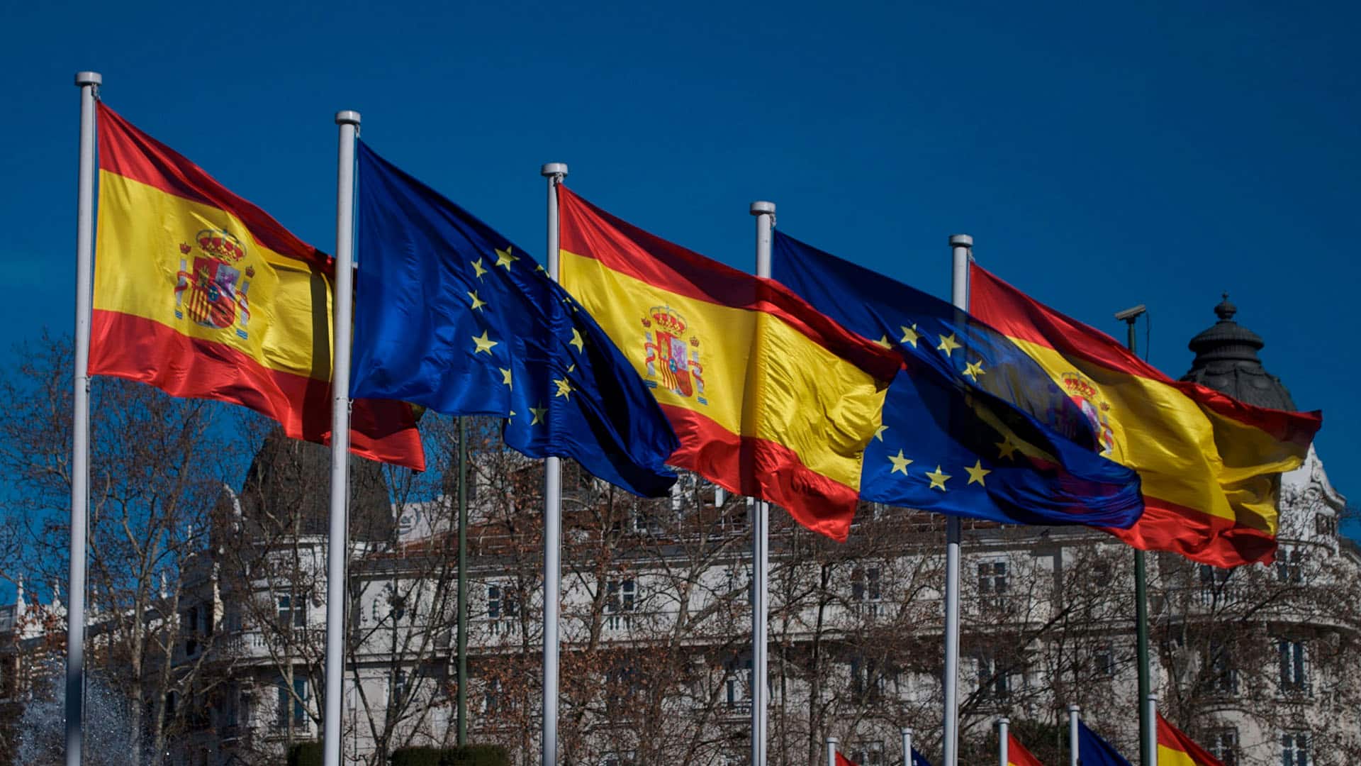 Banderas de España y de la Unión Europea ondeando en la plaza de Cánovas del Castillo (Plaza de Neptuno) en Madrid. Tras los árboles, el edificio del Hotel Ritz. Foto: acho Arenas (CC BY-NC-SA 2.0).
