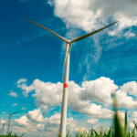 Wind turbine in the foreground of a green field in Villers-le-Bouillet, near Liège (Belgium), under a blue sky with clouds, with more wind turbines visible on the horizon.