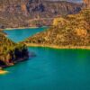Panorámica del embalse de Camarasa (Cataluña), con aguas esmeralda rodeadas de montañas escarpadas y frondosos bosques, bajo un cielo azul que contrasta con algunas nubes. Agua