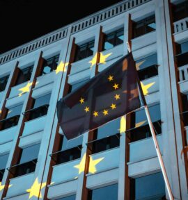 Bandera de la Unión Europea ondea frente a un edificio institucional iluminado con las estrellas de la UE en Berlín (Alemania), durante la noche. Generación Europa