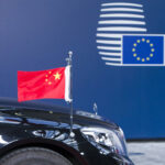 Front of a black luxury car with a miniature Chinese flag in front of a blue background with the logo of the European Council. The photo is from the 2017 China-EU Summit in Brussels, Belgium.