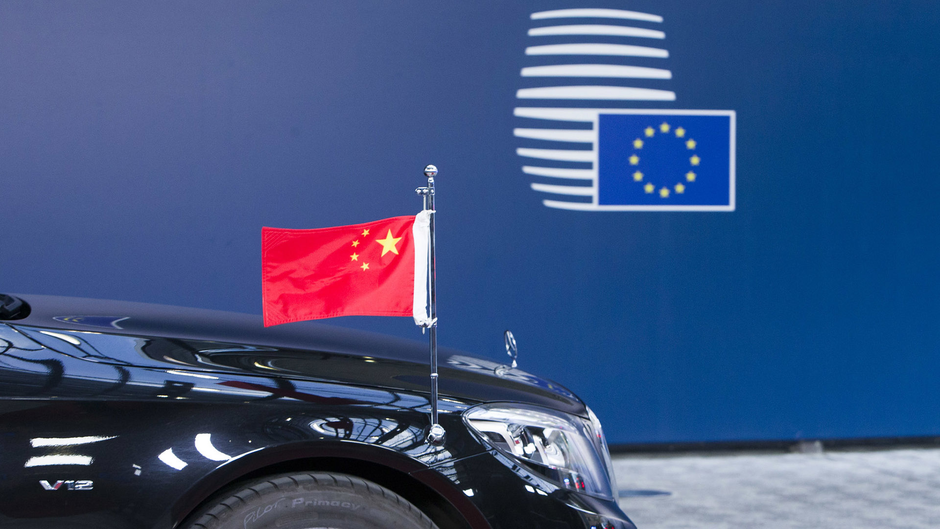 Front of a black luxury car with a miniature Chinese flag in front of a blue background with the logo of the European Council. The photo is from the 2017 China-EU Summit in Brussels, Belgium.