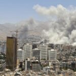 Vista de Tehrán con grandes columnas de humo tras varios edificios altos y grúas de construcción con montañas al fondo, tras un ataque aéreo israelí el 24 de junio de 2025, como parte de la guerra Israel-Irán.