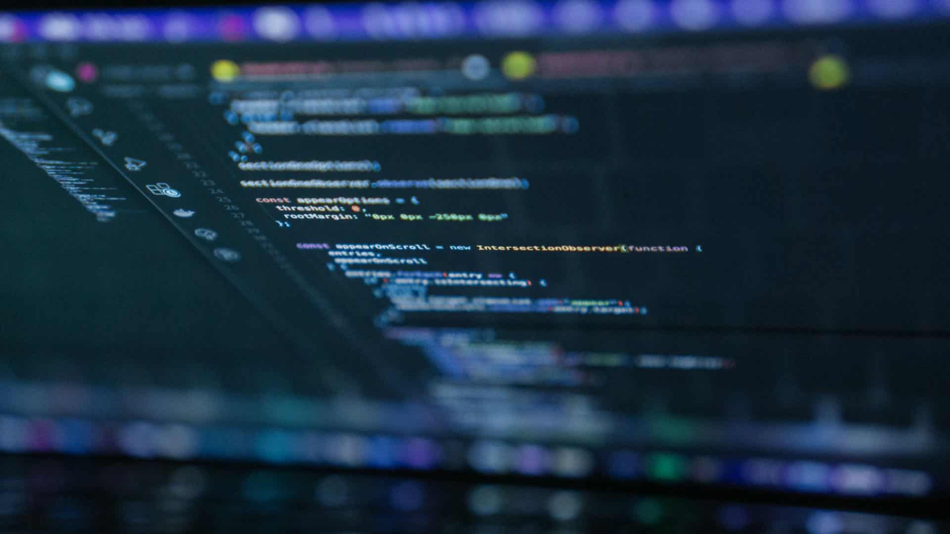 Lines of code on a laptop screen with text highlighted in orange, blue, white, and green on a dark background. Open source