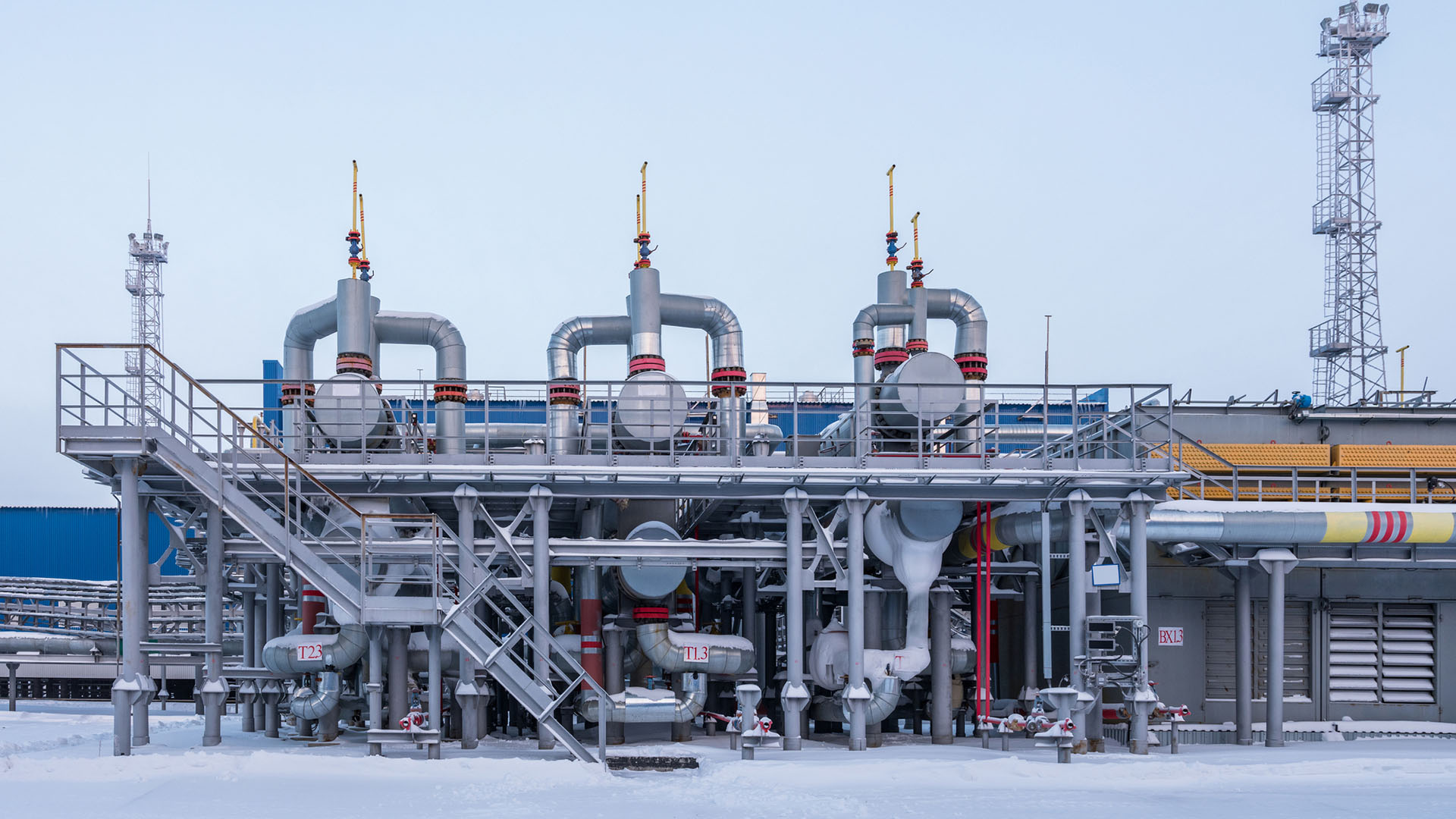 Planta productora de gas cerca de la ciudad de Novi Urengói en el extremo norte de Rusia, uno de los puntos del gasoducto Poder de Siberia 2. La planta está en un entorno nevado, con tres estructuras verticales con válvulas conectadas por tuberías, y una escalera metálica a la izquierda que lleva a una plataforma elevada.