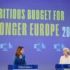 Paula Pinho, portavoz principal de la Comisión Europea (a la izquierda) y Ursula von der Leyen, presidenta de la Comisión Europea (a la derecha) hablando desde los atriles ante la prensa durante el resumen de la reunión semanal de la Comisión sobre el próximo presupuesto de la UE. A la izquierda se asoma una cámara de televisión y al fondo la pantalla azul proyecta el logo de la Comisión en fila y las palabras en inglés “An ambituos budget for a stronger Europe 2028-2034” (un presupuesto ambicioso para una Europa más fuerte 2028-2034).