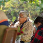 Sushila Karki, former judge and the first female interim prime minister of Nepal elected via Discord, at the Summit for Democracy organised by the US Embassy in Kathmandu in 2021. She is seated with a microphone in her hand next to two other women who are out of focus. In the background, the garden where the event is taking place.